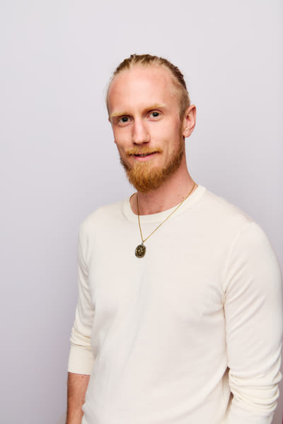 Fredrik Brännlund with a calm half-smile, facing the camera against a pale lilac backdrop